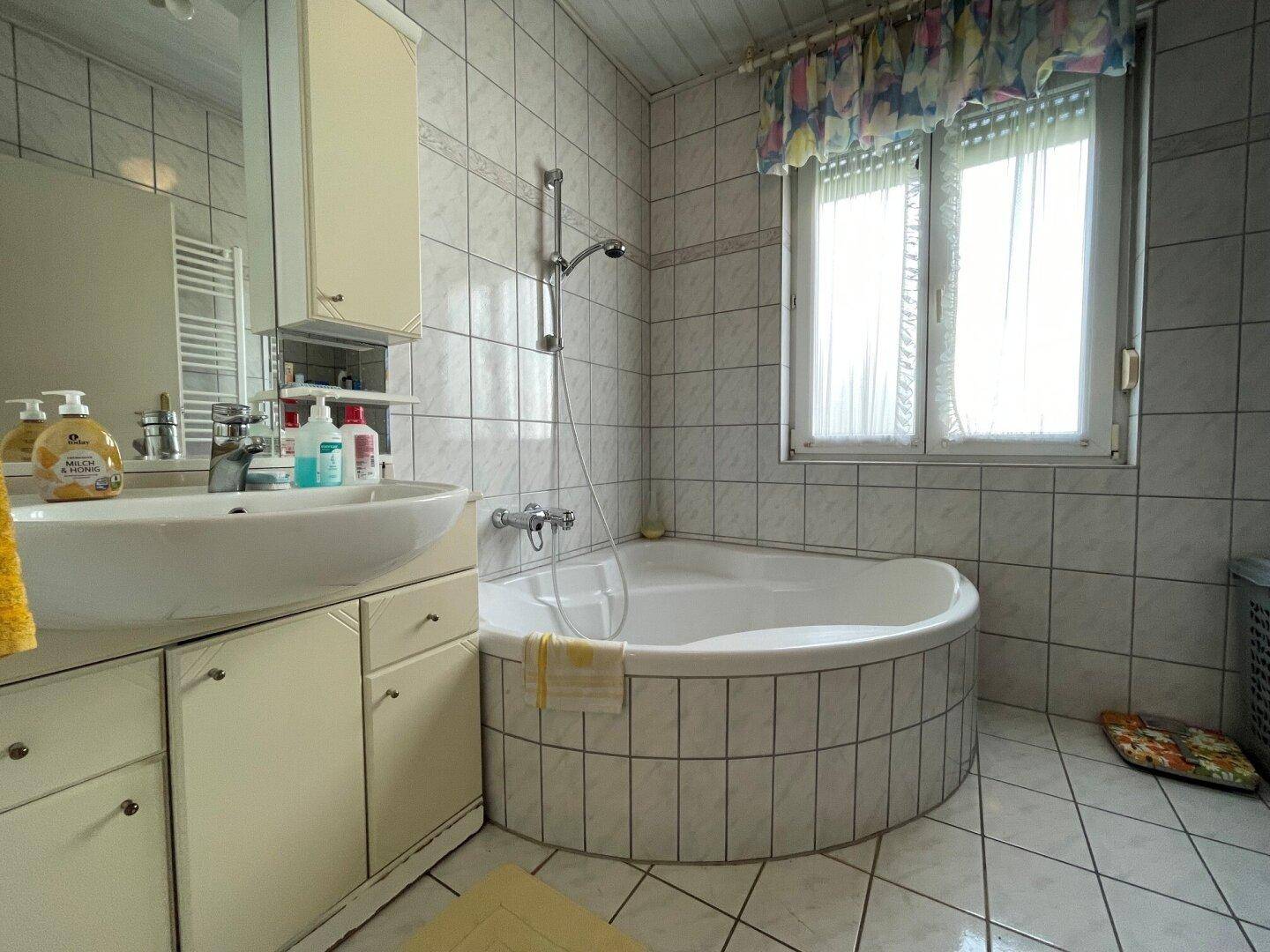Gefliestes Badezimmer mit runder Badewanne, Waschbecken und Fenster für Tageslicht.