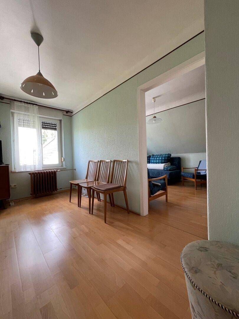 Heller Raum mit Holzboden, Fenster und einfacher Einrichtung, möglicherweise ein Esszimmer.