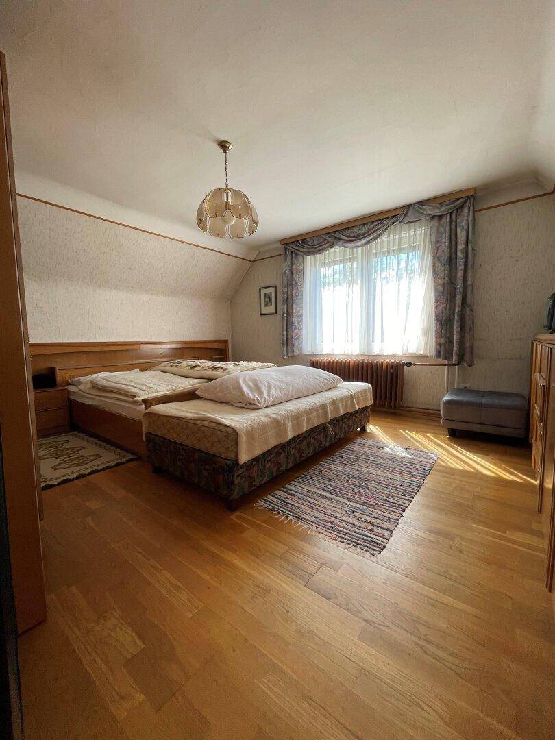 Gemütliches Schlafzimmer mit Holzbett, Parkettboden und Fenster mit Vorhängen unter einer Dachschräge.