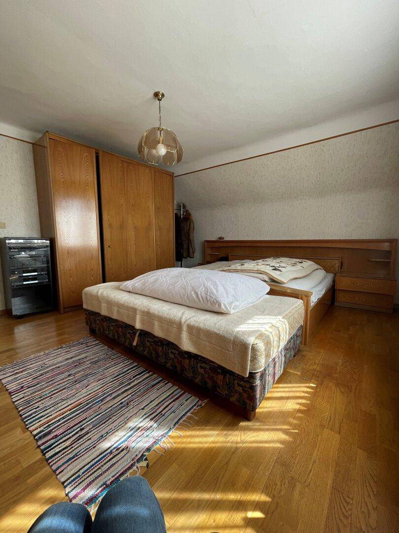 Schlafzimmer mit großem Holzschrank, Parkettboden und gemütlicher Einrichtung unter einer Dachschräge.
