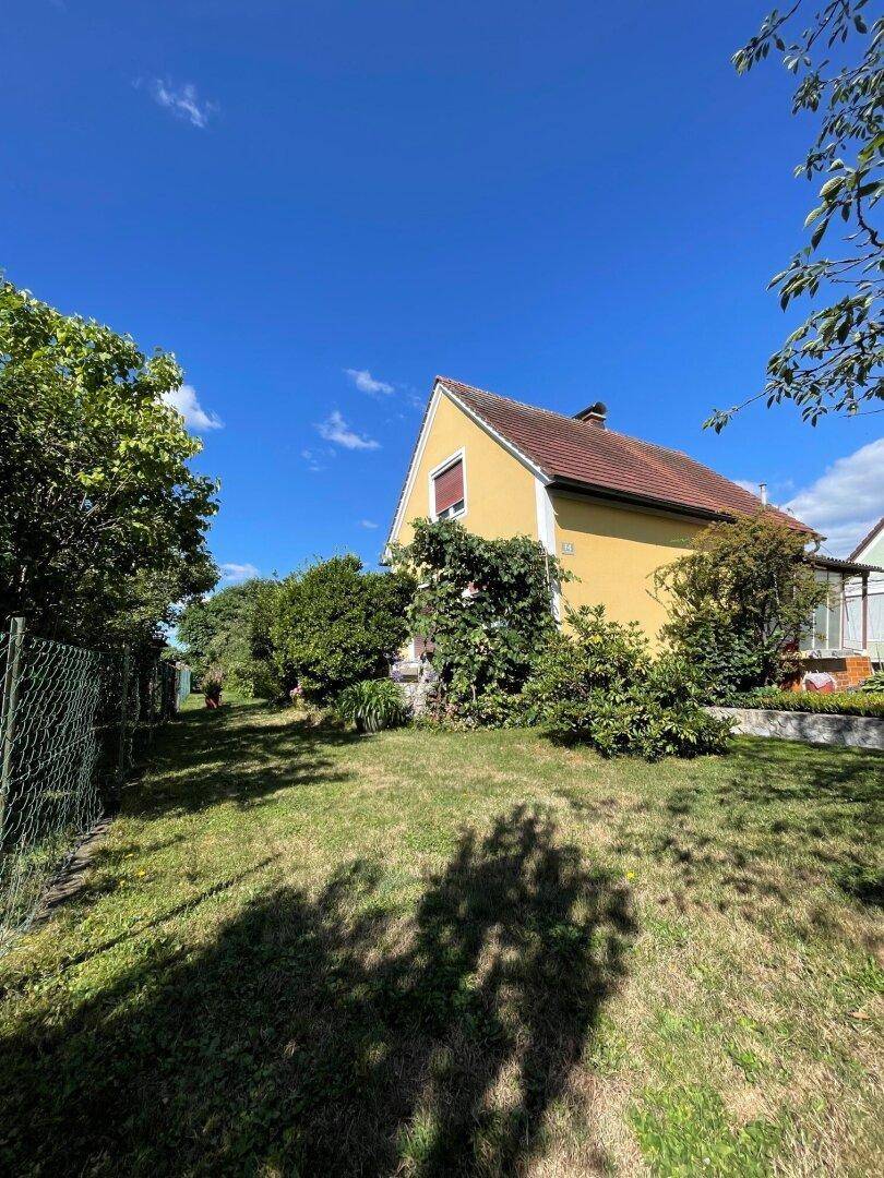 Gelbes Einfamilienhaus mit rotem Ziegeldach, umgeben von einem gepflegten grünen Garten unter blauem Himmel.