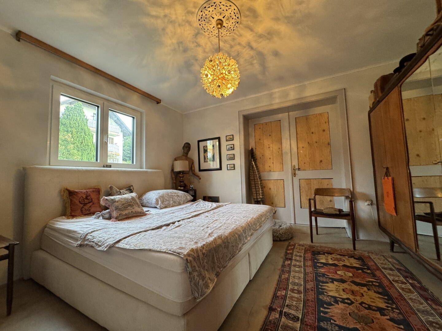Gemütliches Schlafzimmer mit großem Bett, Holztüren, gemustertem Teppich und einem dekorativen Kronleuchter.