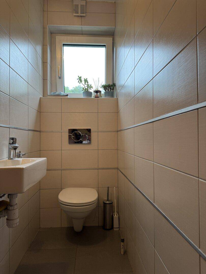 Kleines Gäste-WC mit Toilette, Waschbecken und einem Fenster, komplett gefliest.