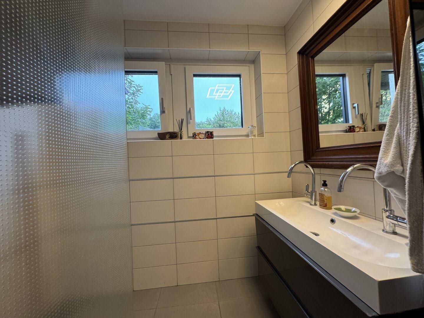 Modernes Badezimmer mit Doppelwaschbecken, großem Spiegel und Fenstern für Tageslicht.