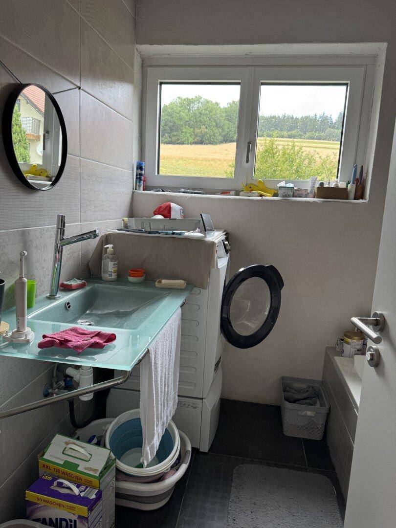 Hauswirtschaftsraum mit Waschmaschine, Waschbecken und einem Fenster mit Blick auf ein grünes Feld.