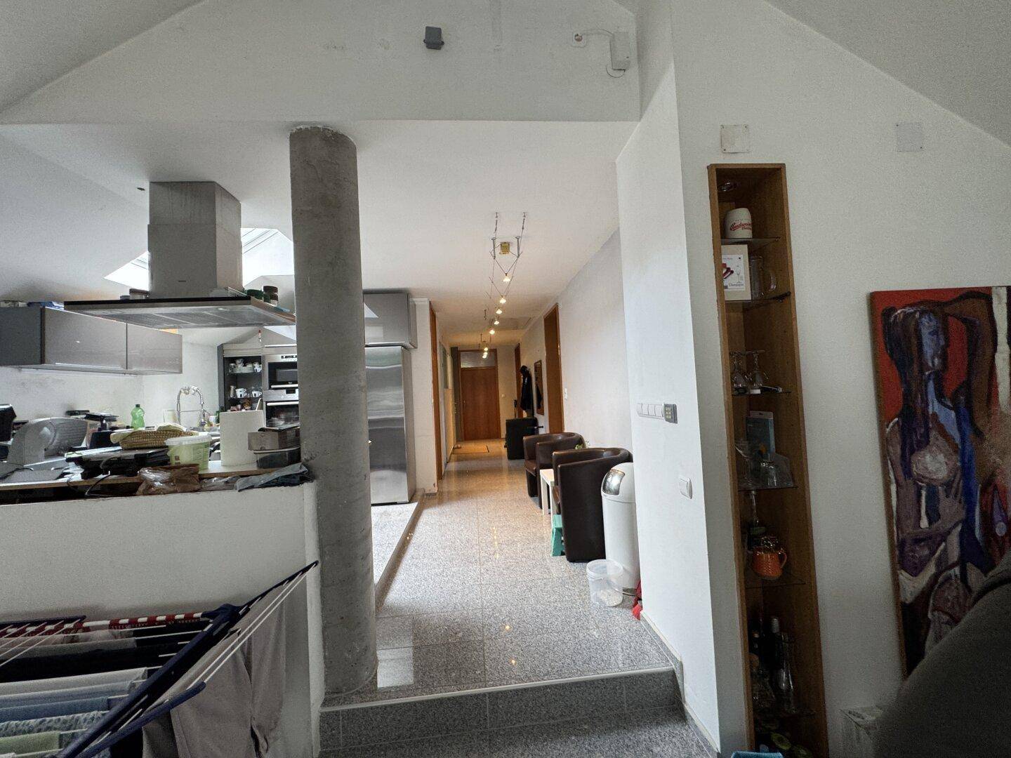 Übergangsbereich von einer Küche zu einem Flur mit Betonsäule und Fliesenboden.