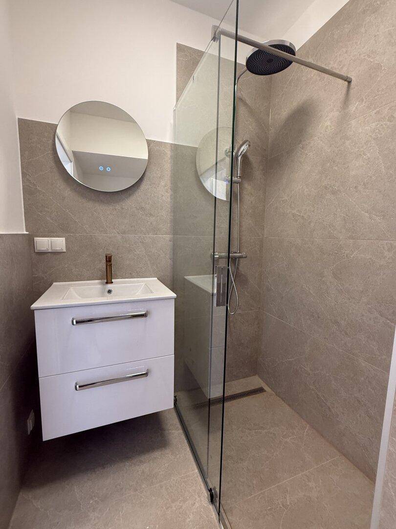 Modernes Badezimmer mit grauen Fliesen, schwebendem Waschtisch und begehbarer Regendusche.