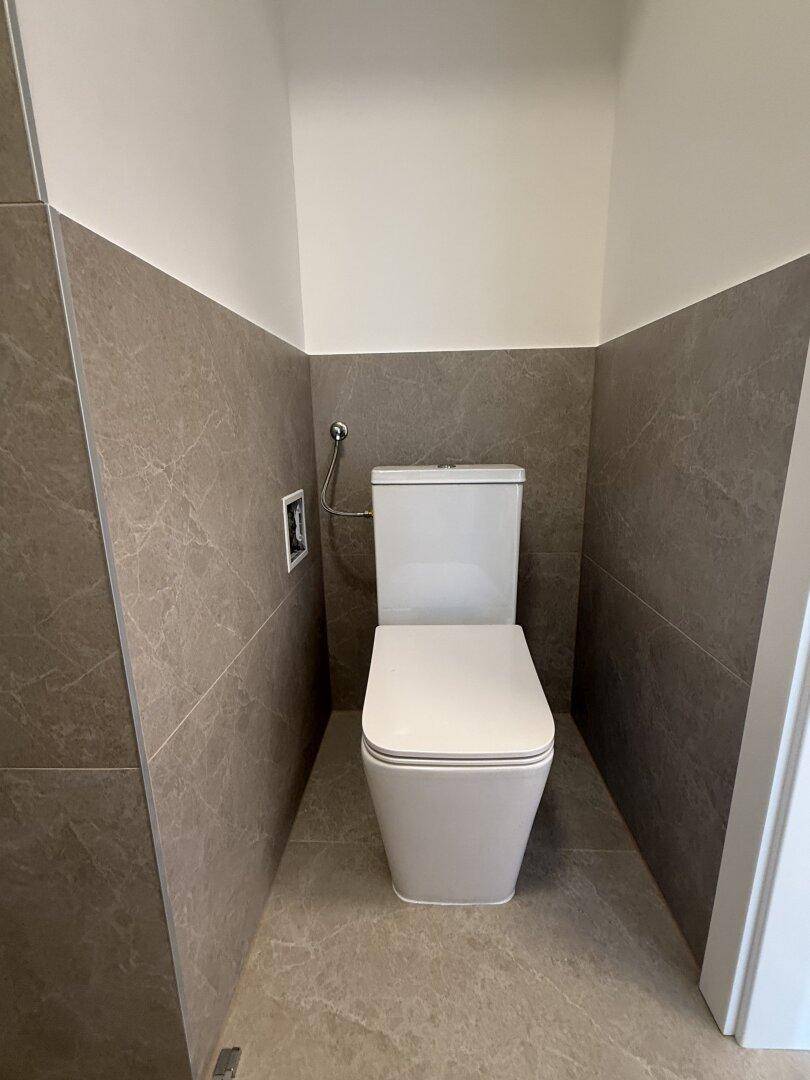 Modernes separates WC mit grauen Fliesen und einer zeitgemäßen Toilette.