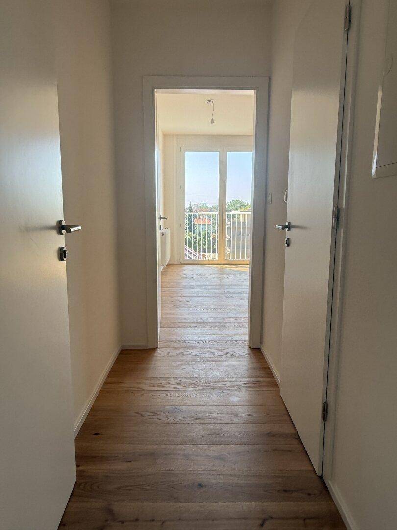 Heller Flur mit Holzboden, der zu einem lichtdurchfluteten Zimmer mit Balkonzugang führt.