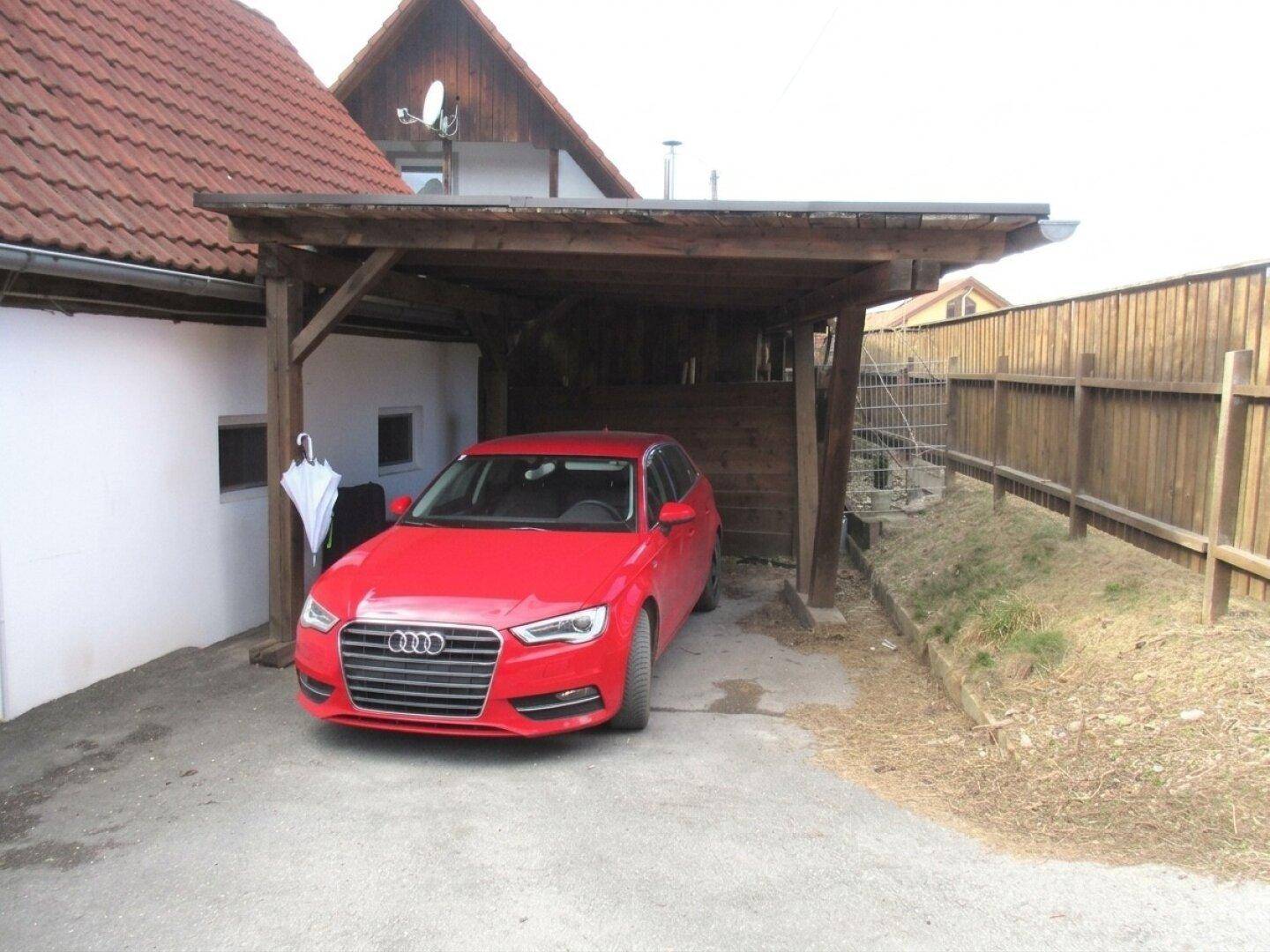 Überdachter Stellplatz für ein Fahrzeug unter einem Holzcarport neben dem Haus.