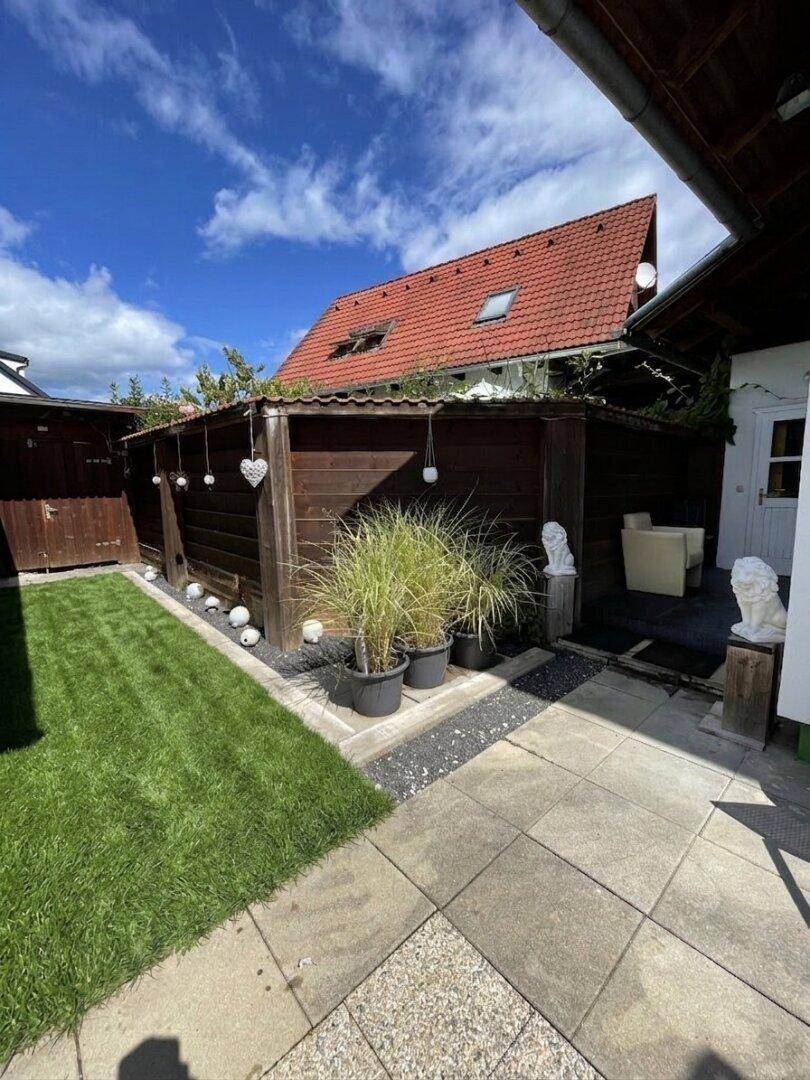 Gepflegter Gartenbereich mit Rasenfläche, gepflastertem Weg und Holzzaun unter blauem Himmel.