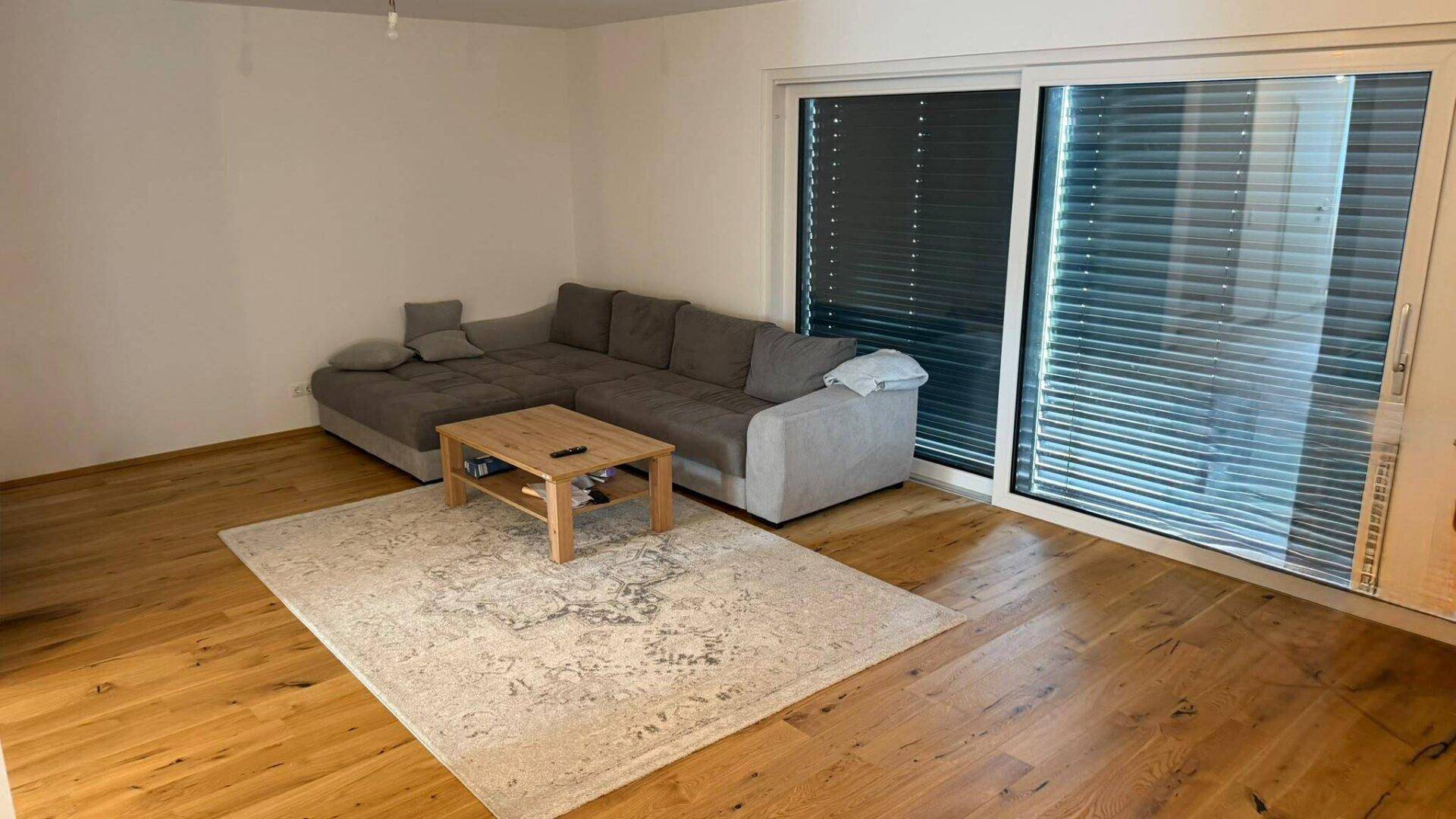 Helles Wohnzimmer mit großem Ecksofa, Holzboden und Zugang zu einer großen Fensterfront.