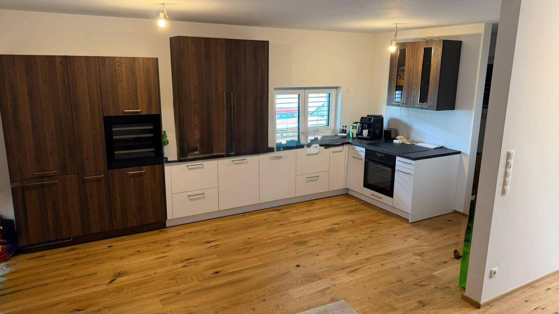 Moderne Einbauküche mit dunklen Holzschränken, weißen Unterschränken und Holzboden.