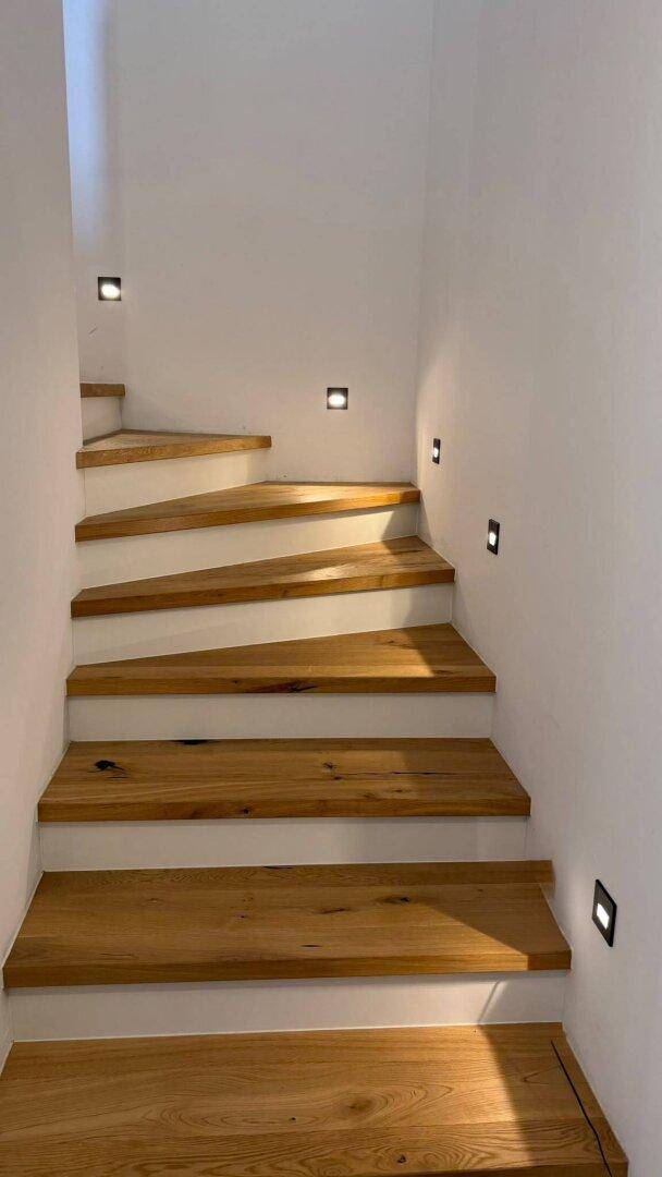 Moderne Holztreppe mit integrierter Wandbeleuchtung, die zu den oberen Etagen führt.