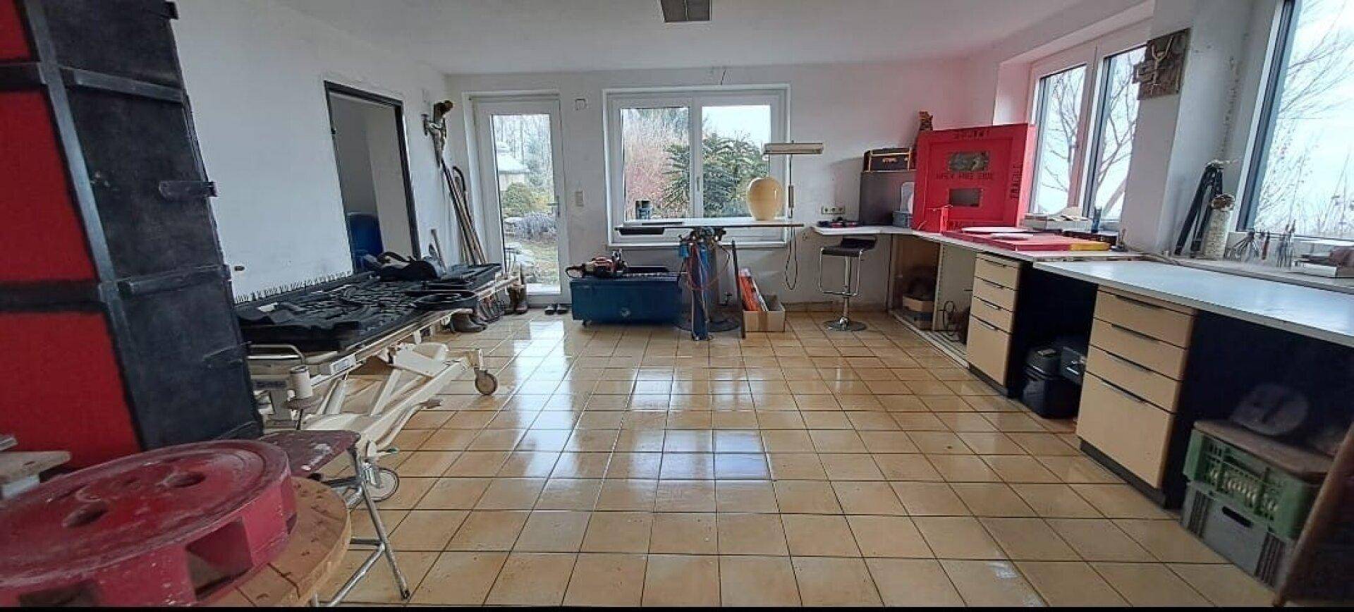 Großer Raum mit Fliesenboden, Fenstern und verschiedenen Arbeitsbereichen oder Lagerflächen.