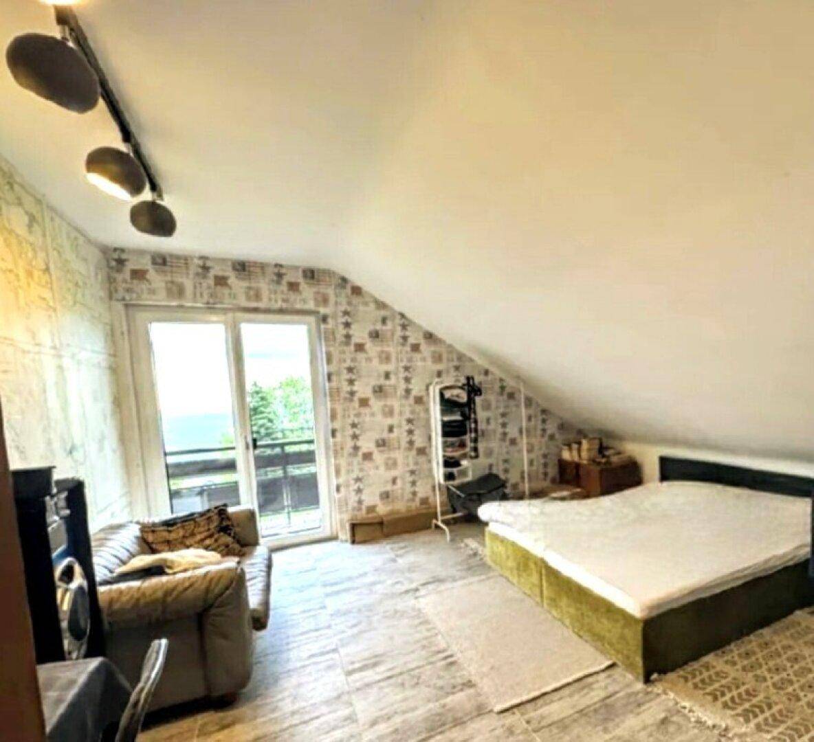 Schlafzimmer im Dachgeschoss mit schrägen Wänden, Sofa und Zugang zu einem Balkon.