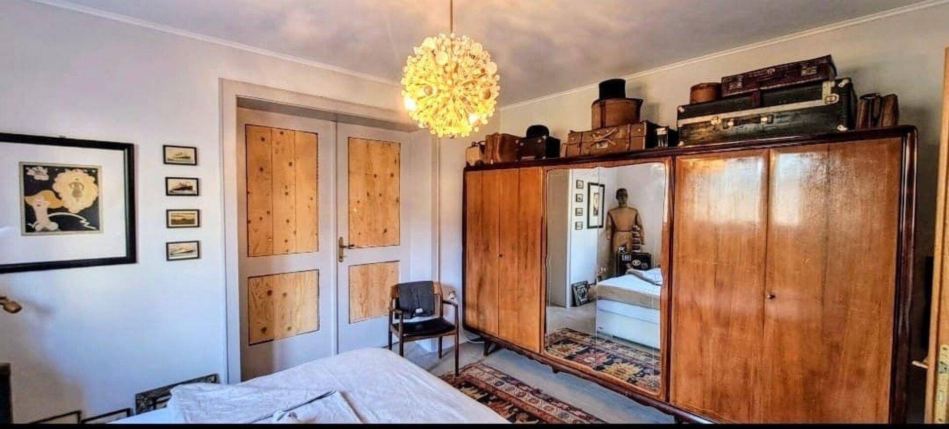 Schlafzimmer mit großem Holzschrank, Doppelbett und dekorativer Deckenleuchte.