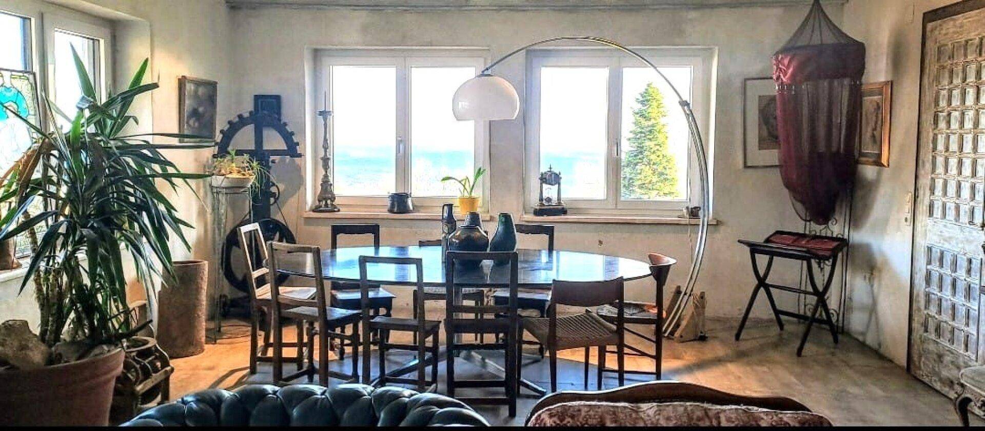 Esszimmer mit großem Esstisch, vielen Fenstern und Blick auf die Umgebung.