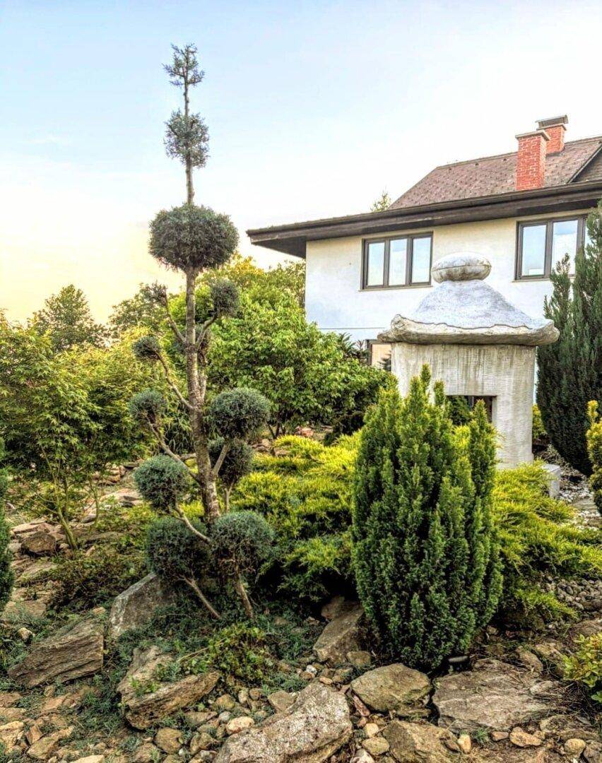 Gepflegter Garten mit Zierbäumen, Felsen und üppiger Bepflanzung vor dem Haus.
