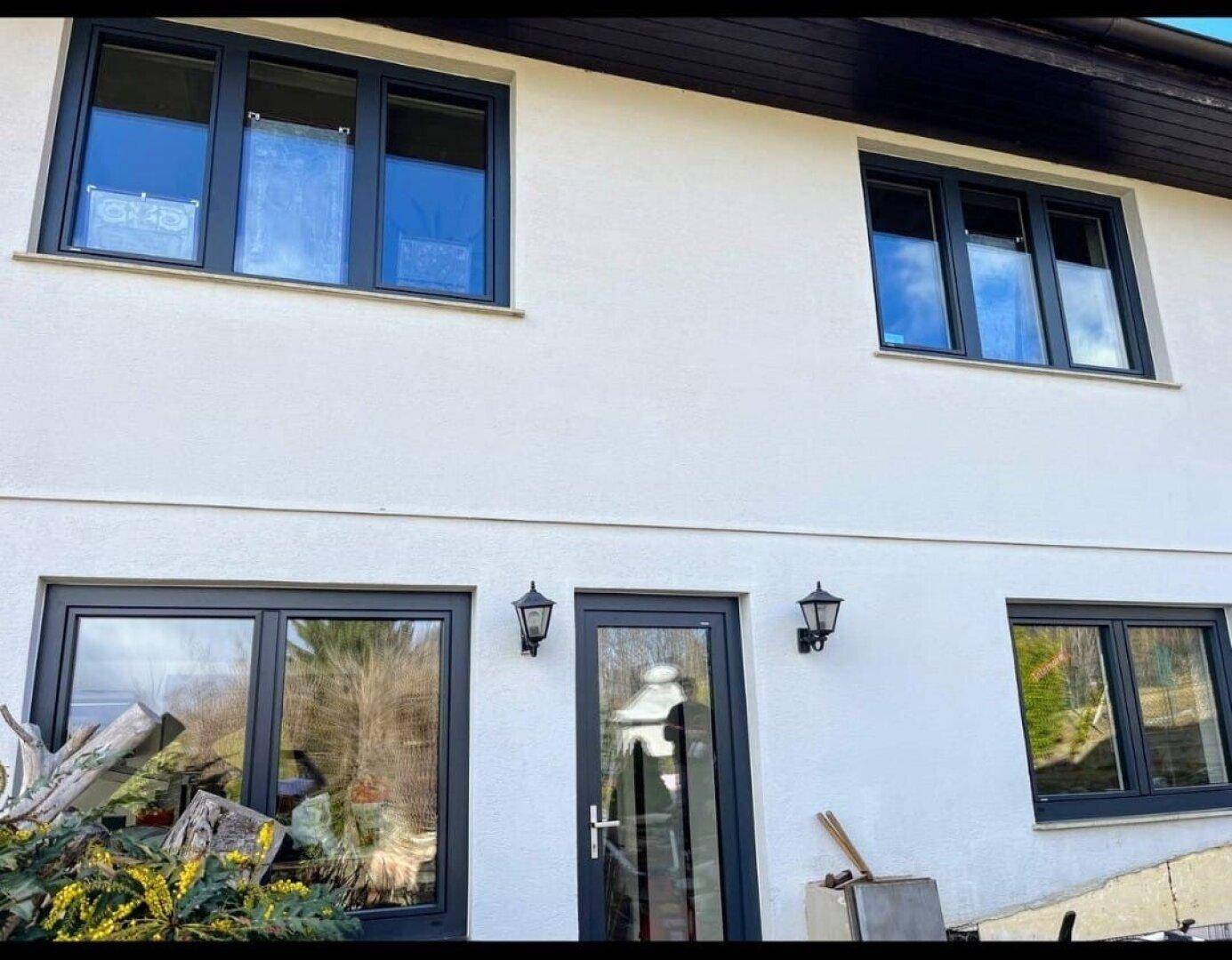 Moderne Hausfassade in Weiß mit dunklen Fensterrahmen und Eingangstür.