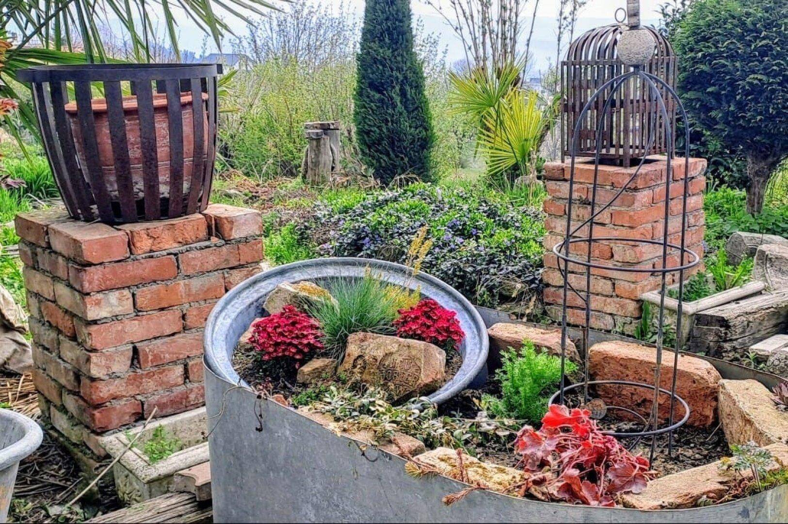 Kreativ gestalteter Gartenbereich mit Hochbeeten, Ziegelsteinen und vielfältigen Pflanzen.