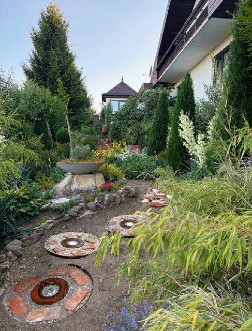 Geschwungener Gartenweg mit dekorativen Trittsteinen und üppiger Bepflanzung neben dem Haus.