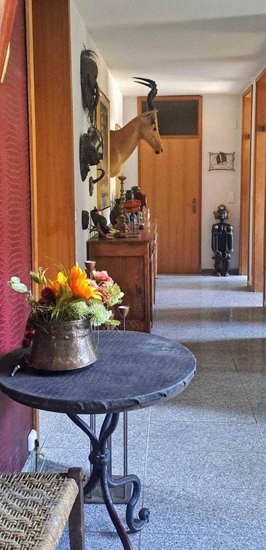Langer Flur mit Holztüren, Fliesenboden und einem Beistelltisch mit Blumen.