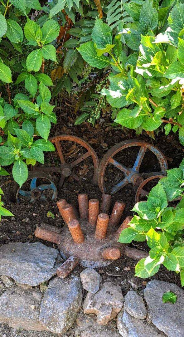 Rustikale Dekoration mit alten Wagenrädern und Holzstücken inmitten von Grünpflanzen im Garten.