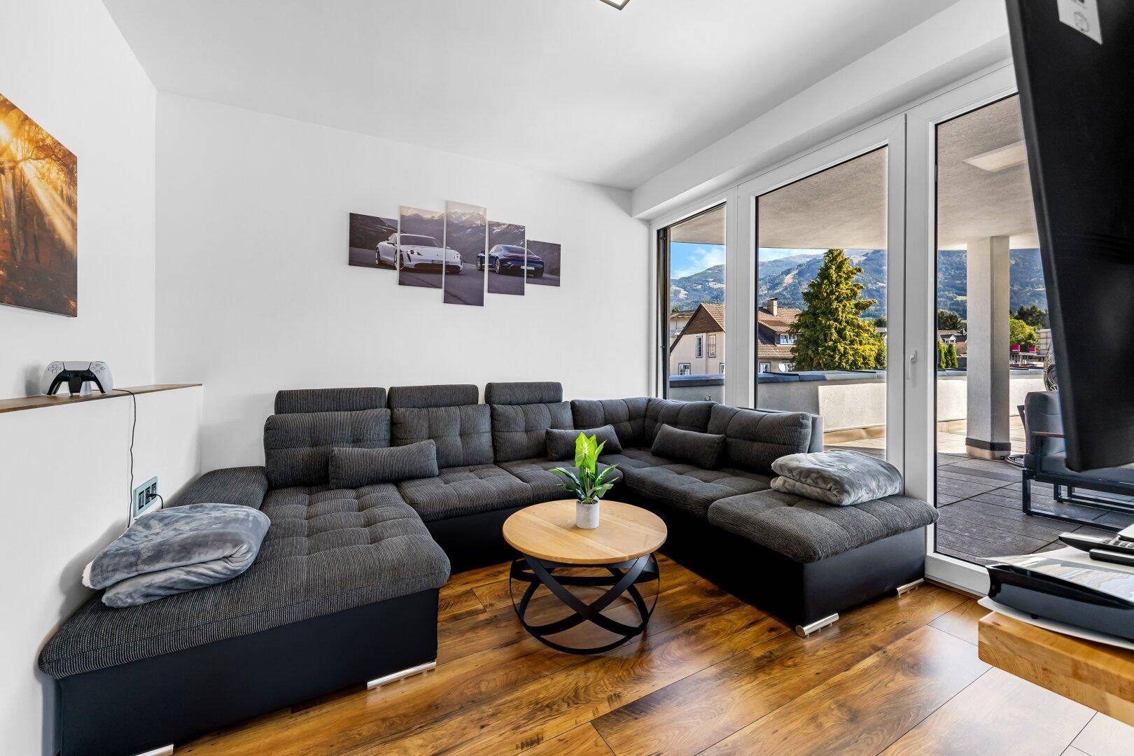 Gemütliches Wohnzimmer mit großem Ecksofa, Holzboden und Zugang zur Terrasse mit Bergblick.
