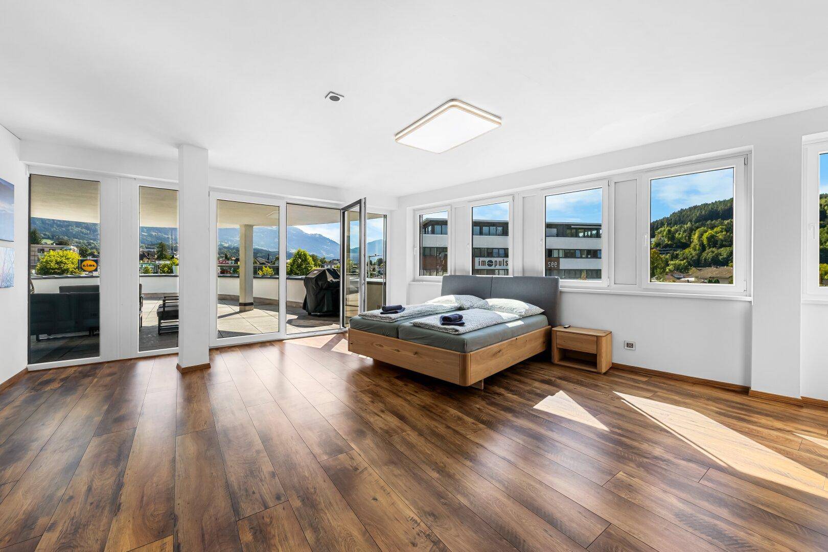 Helles Schlafzimmer mit Holzbett, großen Fenstern und direktem Zugang zur Terrasse mit Bergblick.