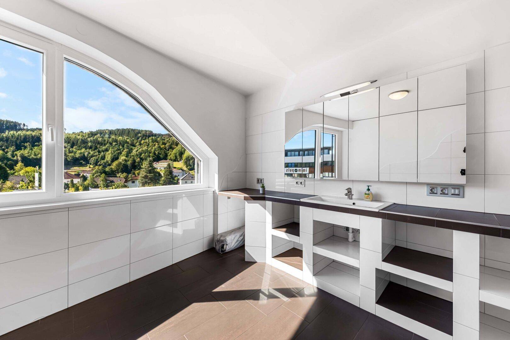 Helles Badezimmer mit Doppelwaschbecken, großem Fenster und weitem Blick ins Grüne.