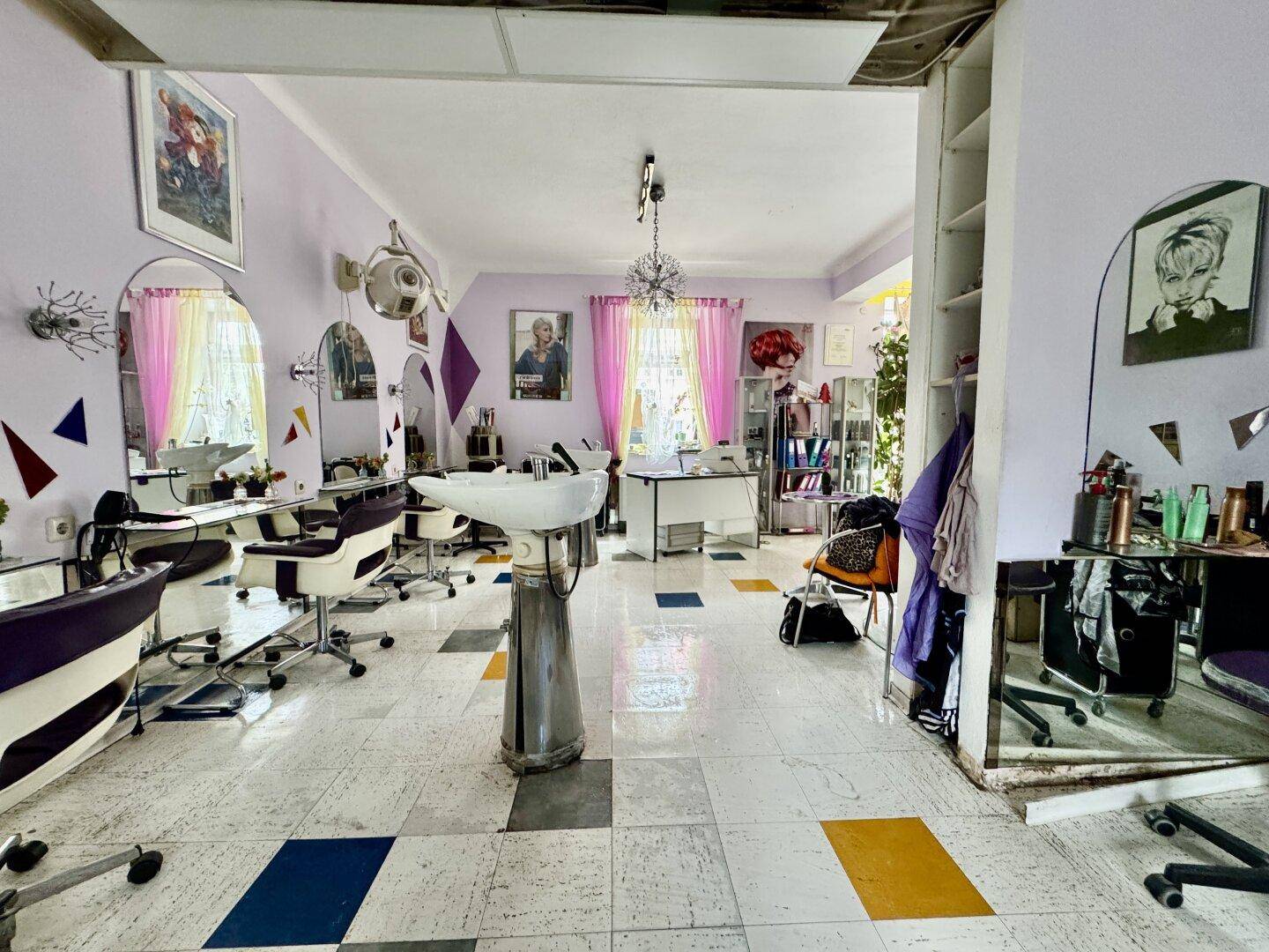 Blick in den Friseursalon mit weiteren Styling-Bereichen, Regalen und Fenstern mit Vorhängen.