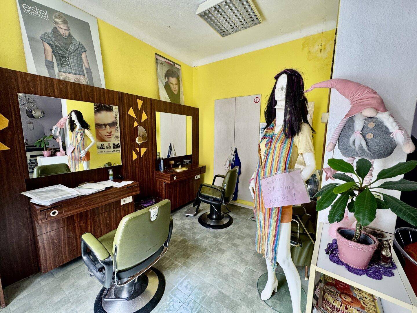 Separater Bereich des Salons mit gelben Wänden, Holzmöbeln und einem Schaufensterpuppen-Display.