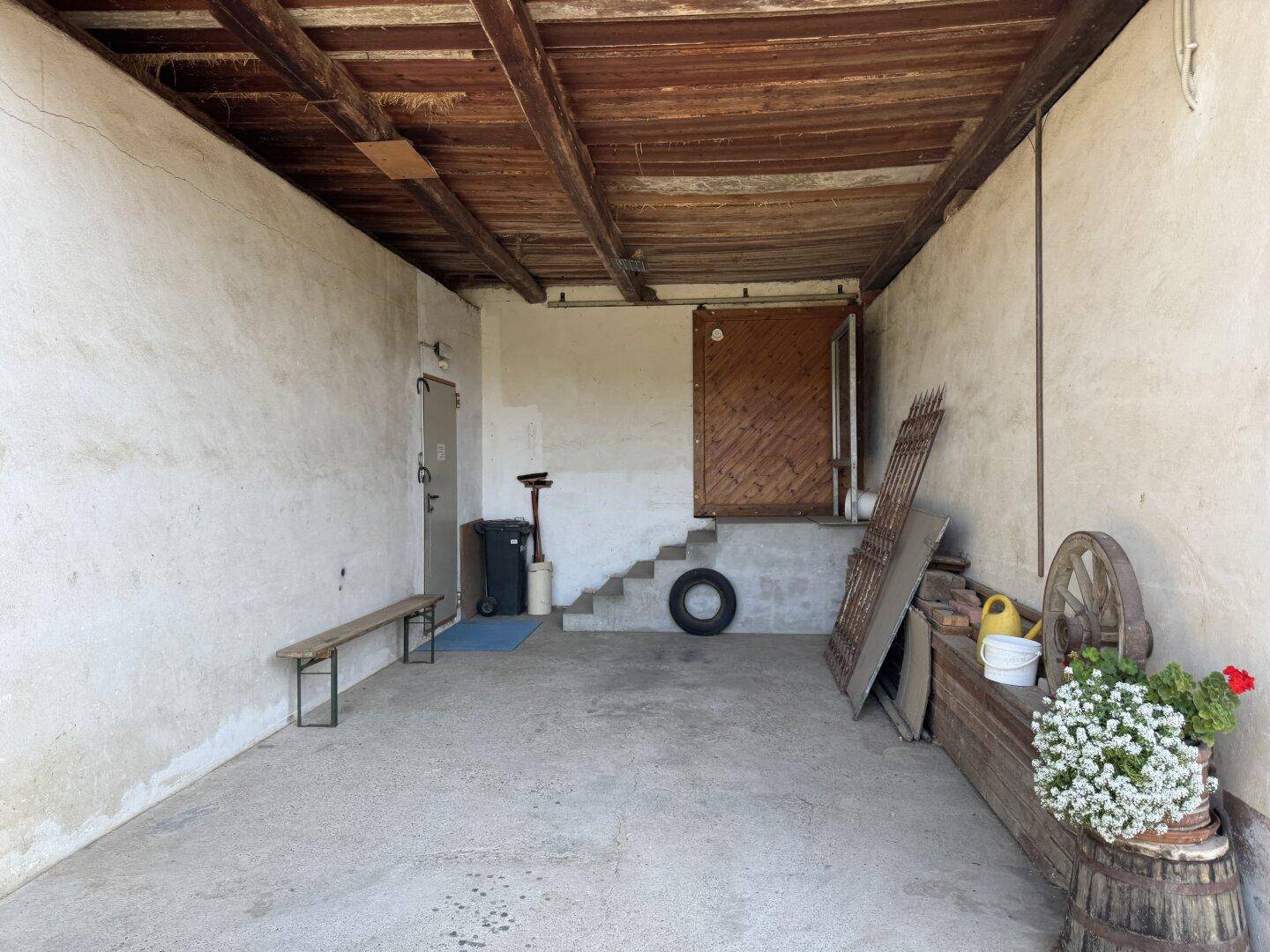 Abstellraum mit Betonboden, Holzbalkendecke und Zugang zu einem weiteren Bereich.