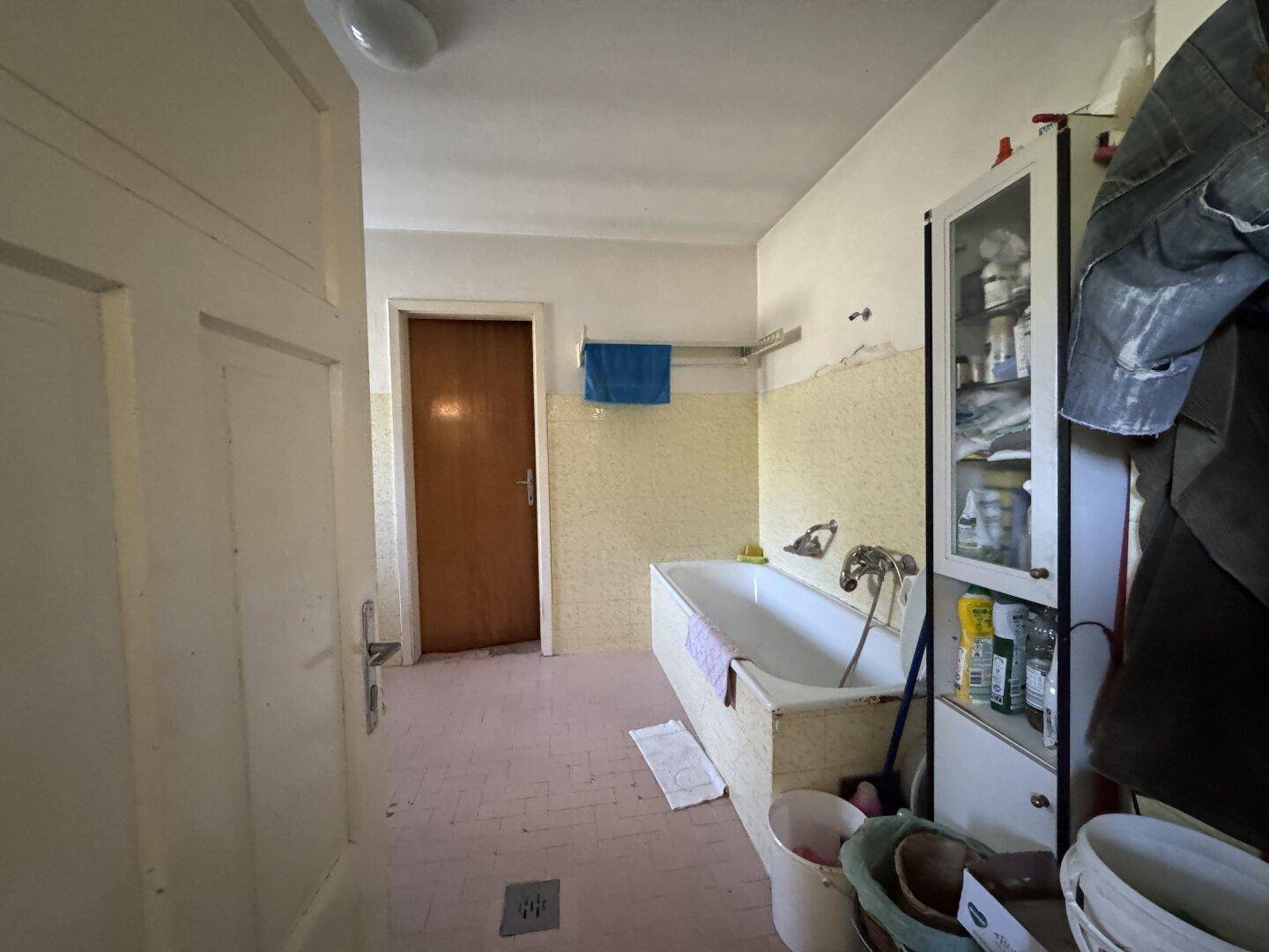 Badezimmer mit Badewanne, gelben Wandfliesen und rosa Bodenfliesen im 80er-Jahre-Stil.
