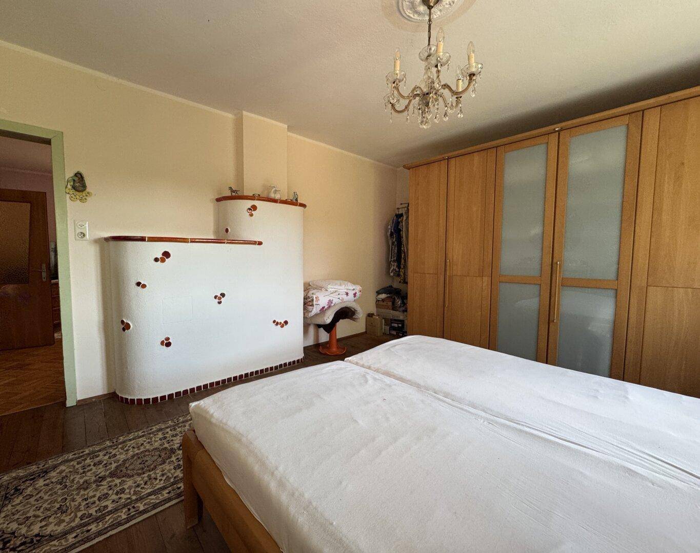 Schlafzimmer mit Holzboden, traditionellem Kachelofen und großem Kleiderschrank.