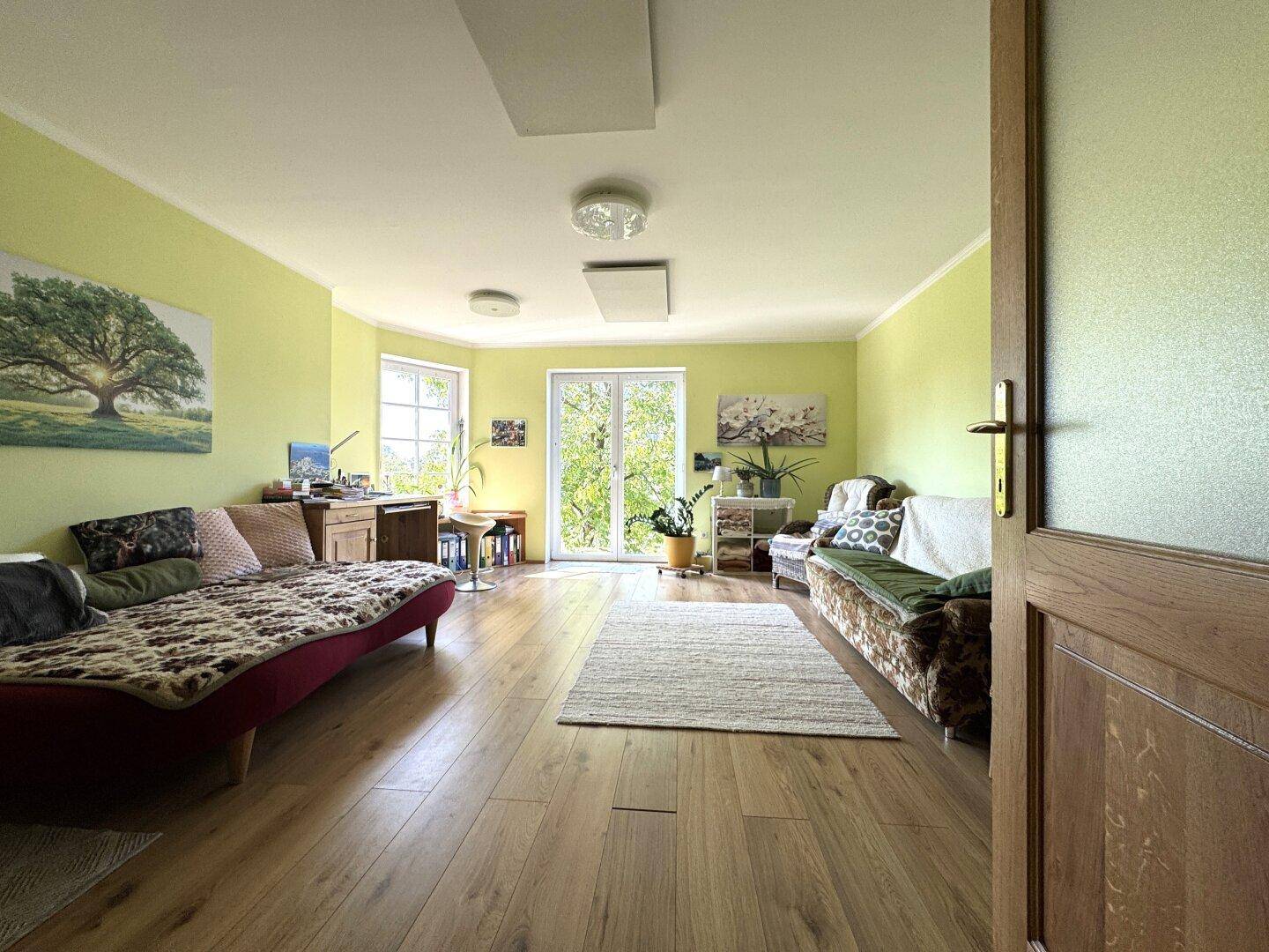 Helles Wohnzimmer mit Holzboden, grünen Wänden und Zugang zu einem Balkon.