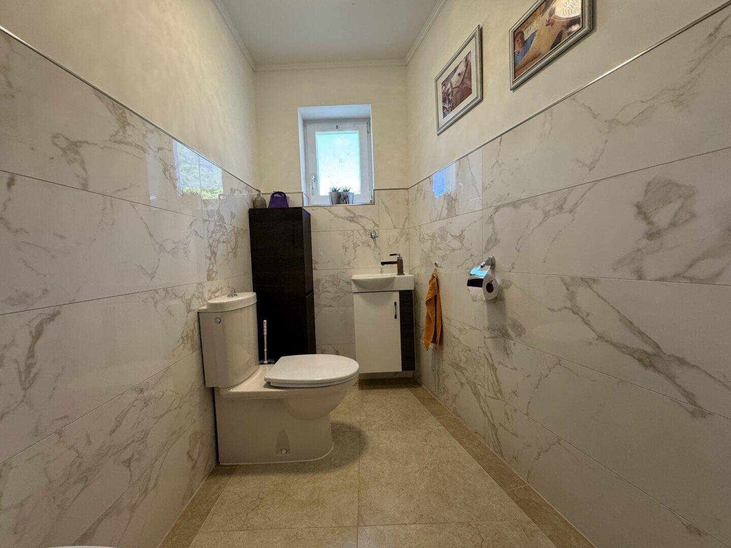 Modernes Gäste-WC mit Marmorfliesen, kleinem Waschbecken und Fenster für Tageslicht.