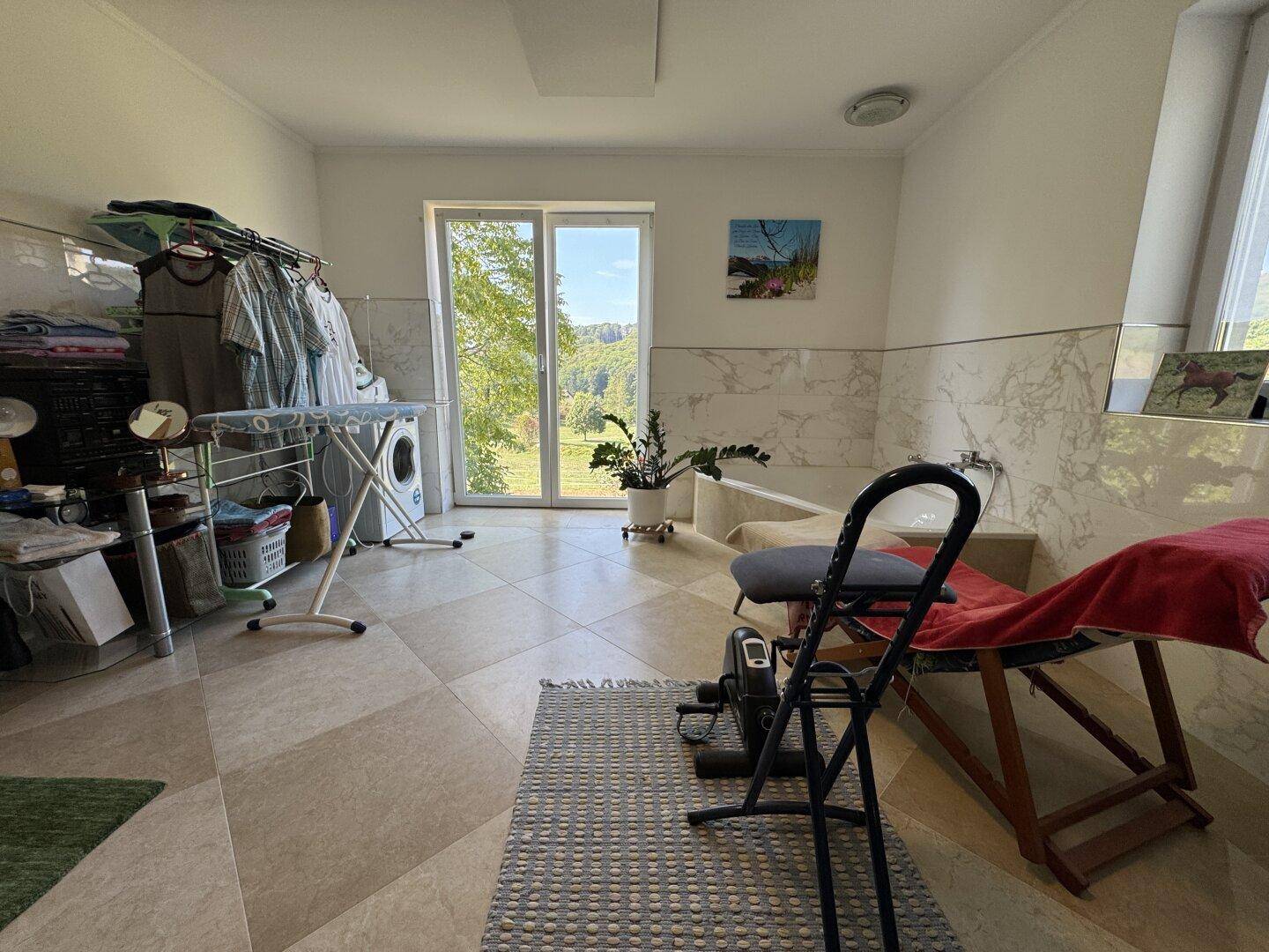 Geräumiges Badezimmer mit Badewanne, Fliesenboden und Zugang zu einem Außenbereich.