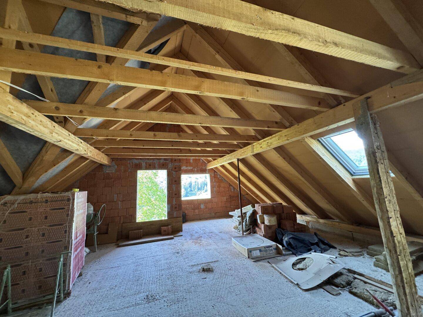 Unausgebauter Dachboden mit sichtbaren Holzbalken und Ziegelwänden, bereit für den Ausbau.