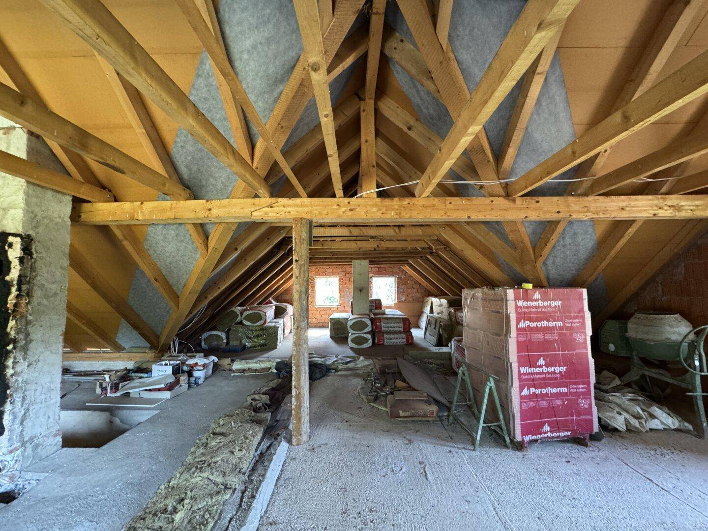 Großer unausgebauter Dachboden mit Holzdachstuhl und Baumaterialien, ideal für zukünftige Projekte.