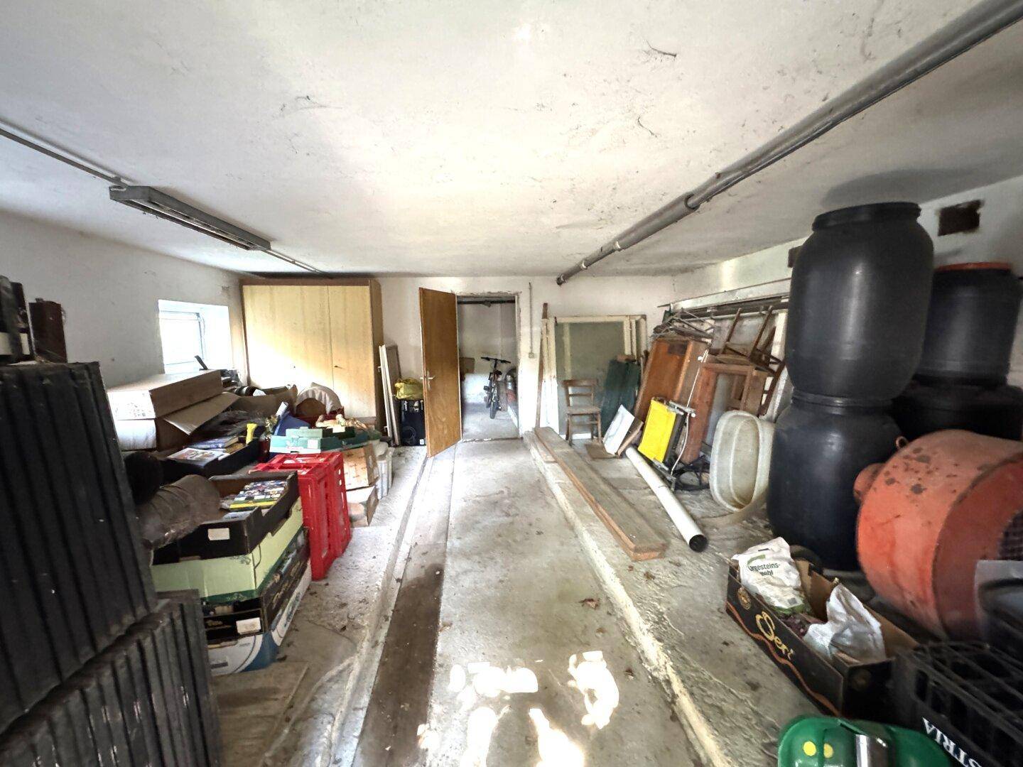 Geräumiger Lagerraum oder Garage mit Betonboden und verschiedenen Gegenständen, ideal für Abstellzwecke.