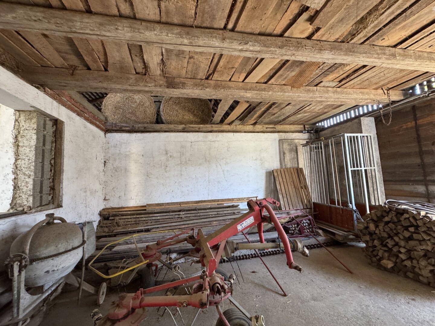 Innenraum einer Scheune mit sichtbaren Holzbalken, Heuballen und landwirtschaftlichen Geräten.