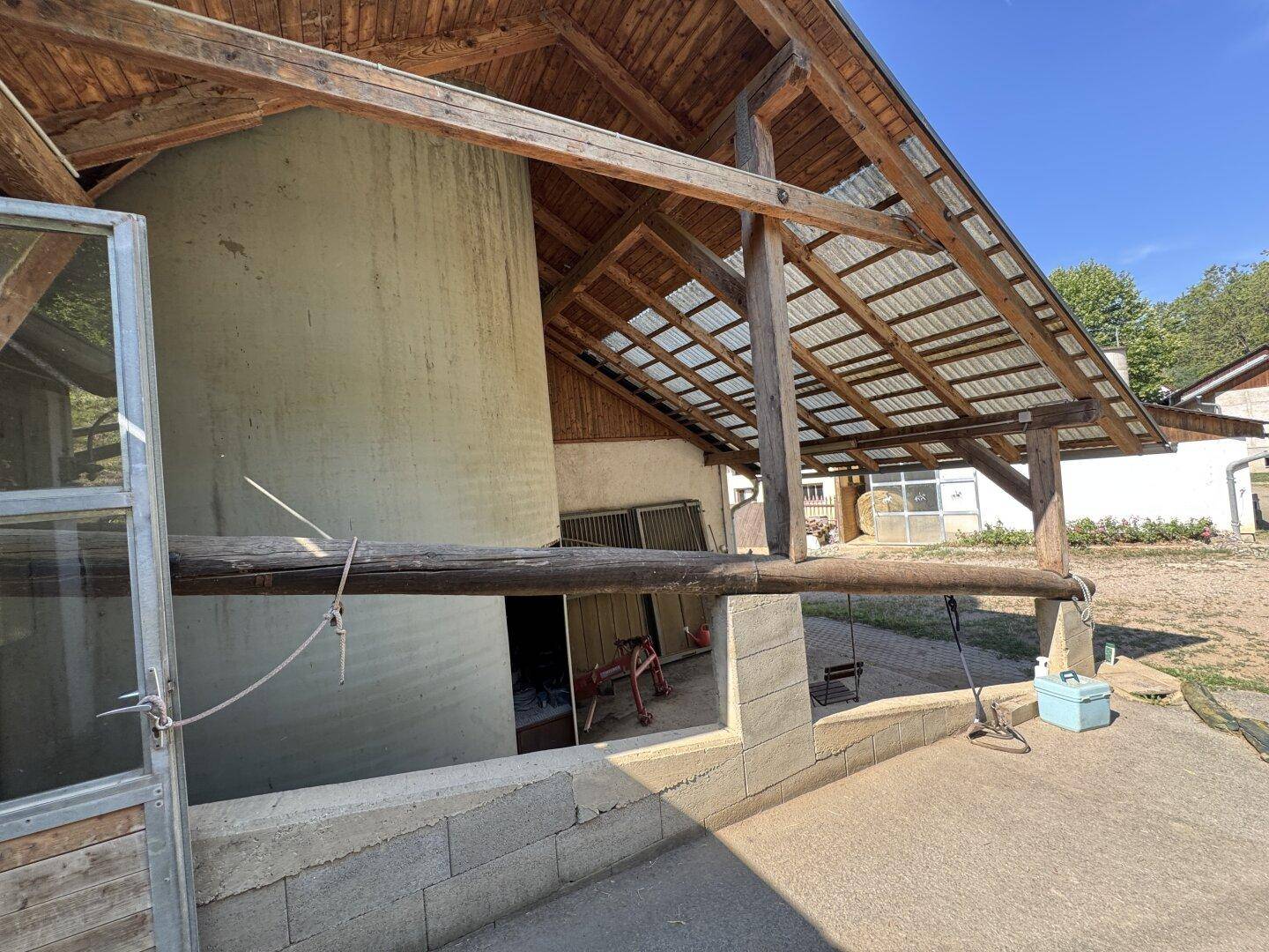 Außenansicht eines Silos und eines überdachten Bereichs mit Holzbalken, der zu einem offenen Platz führt.