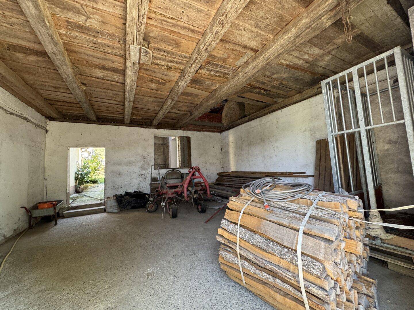 Rustikaler Innenraum mit Holzbalkendecke und gelagertem Brennholz, ideal als Abstellraum.