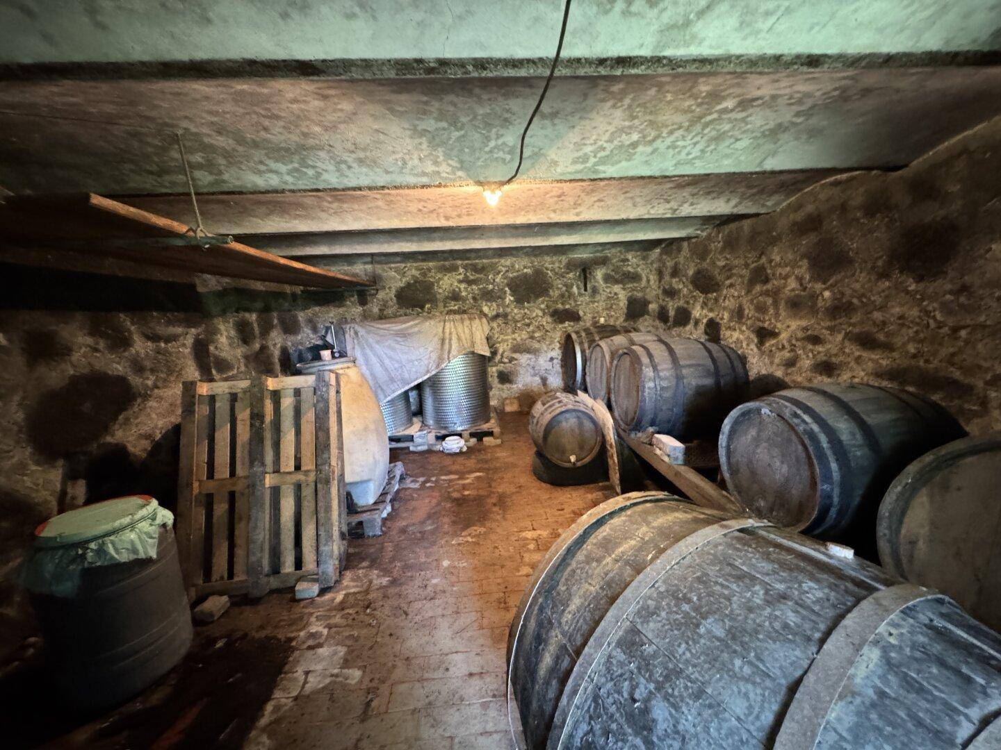 Historischer Weinkeller mit Steinfundament und Holzfässern, ideal zur Lagerung von Wein.