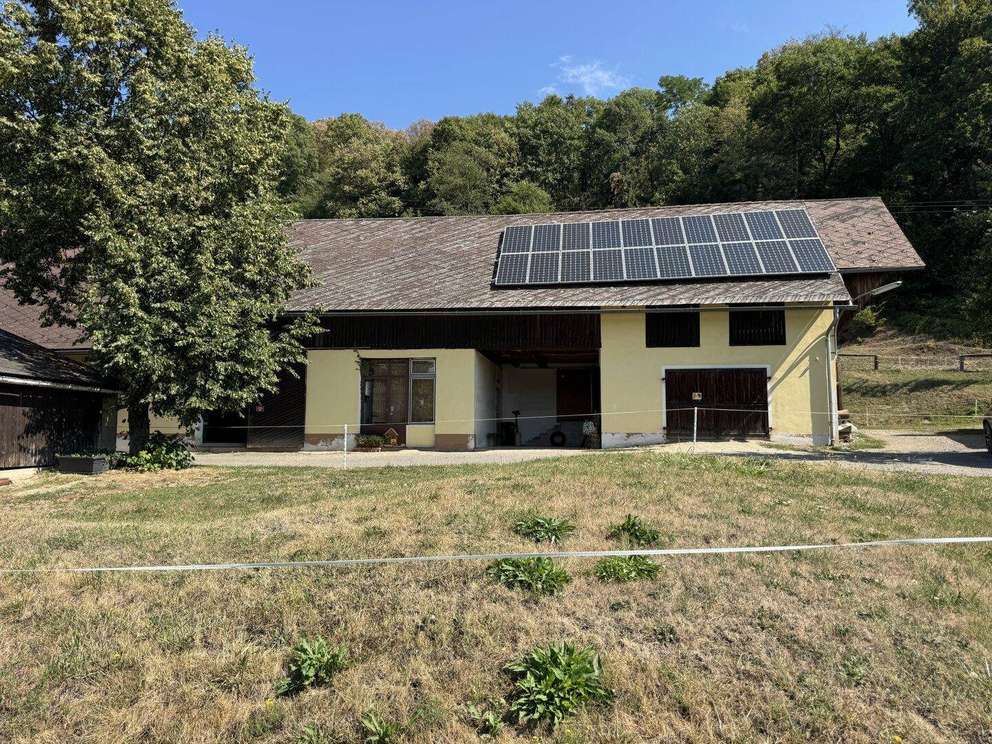 Ländliches Gebäude mit Photovoltaikanlage auf dem Dach, umgeben von einer grünen Wiese.