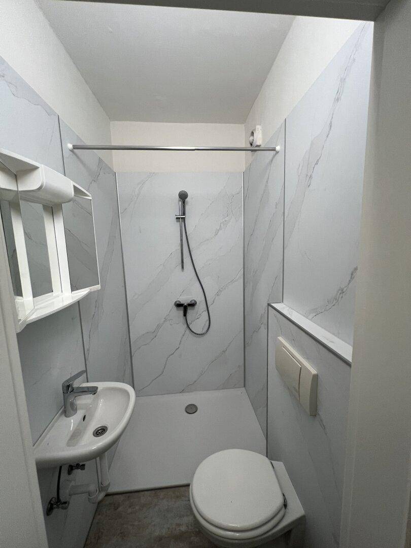 Kompaktes Badezimmer mit Duschbereich, wandhängendem WC und Waschbecken, ausgestattet mit modernen Fliesen.
