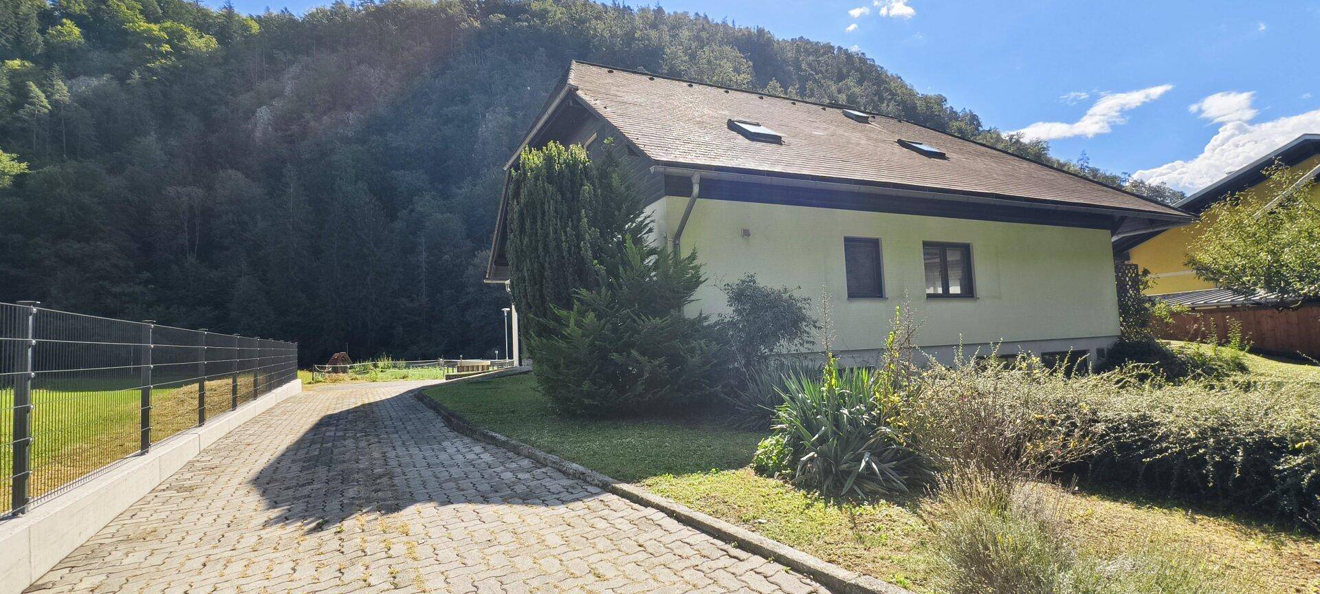 Seitenansicht des Hauses mit gepflasterter Auffahrt und grüner Umgebung.