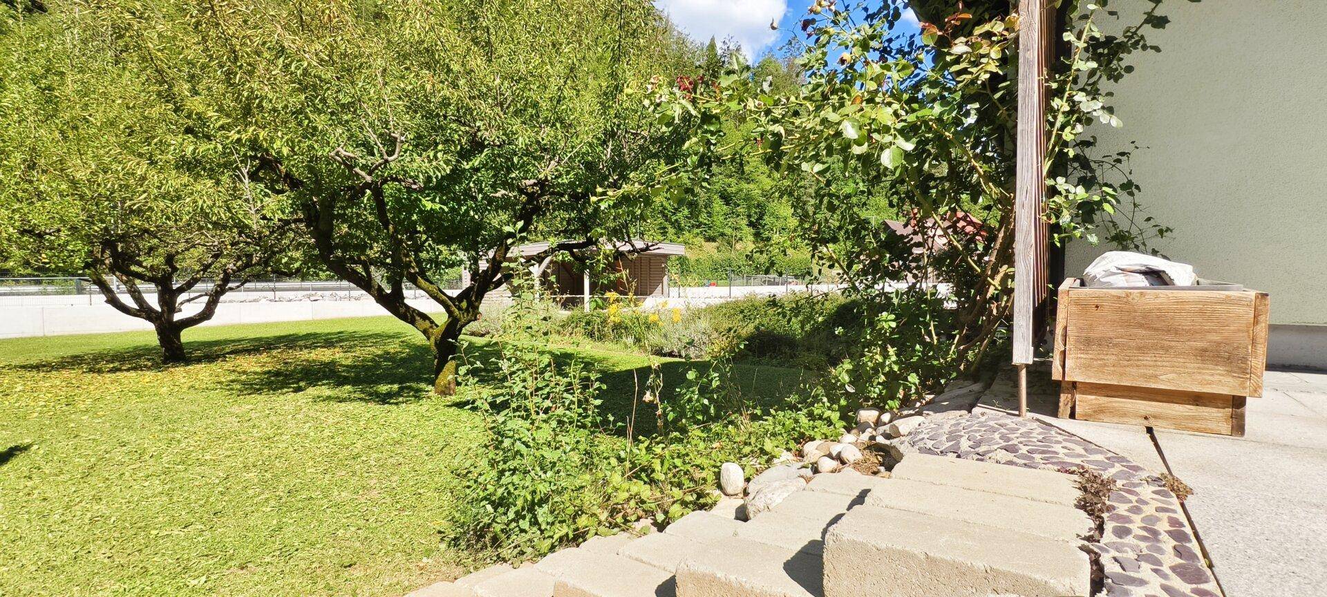 Terrasse mit Steinstufen und Blick auf den gepflegten Garten mit Obstbäumen.
